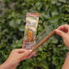 A person holds a packaged cone of Blazy Susan tea leaf cones in their hands, with a background of green ivy leaves.