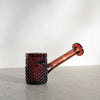 Amber glass hand pipe with a textured bowl on a light gray surface