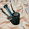 Glass hand pipe with textured design on a beige fabric background