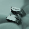 Two metallic silver rings with a sleek, modern design and the brand name 'Krush' engraved on one, displayed on a soft, draped sage green fabric background.