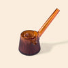 An amber brown ribbed glass smoking pipe with a long angled stem by NWTN Home, shown on a solid light beige background.