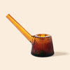 An amber glass smoking pipe with a ribbed, conical bowl and a long, curved stem by NWTN Home, shown on a solid light beige background.