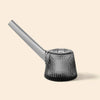 A modern, ribbed glass water pipe by NWTN Home with a tapered base and a long angled stem, shown on a solid light beige background.