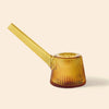A NWTN Home translucent amber glass water pipe with a ribbed conical body and a long angled mouthpiece, shown on a plain warm beige background.