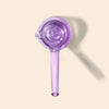 A translucent purple hand pipe with a circular textured head and a long handle, shown on a light beige background with a soft shadow.