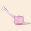 A NWTN Home translucent pink glass water pipe with a ribbed, flared base and a long angled mouthpiece, shown on a solid light beige background.