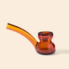 An amber glass water pipe by NWTN Home with a curved stem and a bulbous base, shown on a solid light beige background.