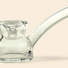 Clear glass water pipe by NWTNH Home with a curved stem and bowl section, photographed on a plain warm beige background.