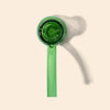 A translucent green glass hand pipe by NWTN Home with a long handle, shown on a warm beige background with a soft shadow.