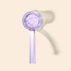 A translucent lavender purple glass hand pipe with a long handle and a circular bowl, shown on a solid light beige background with a soft shadow.