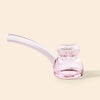 A small pink-tinted glass hand pipe with a curved mouthpiece, photographed on a plain warm cream background.